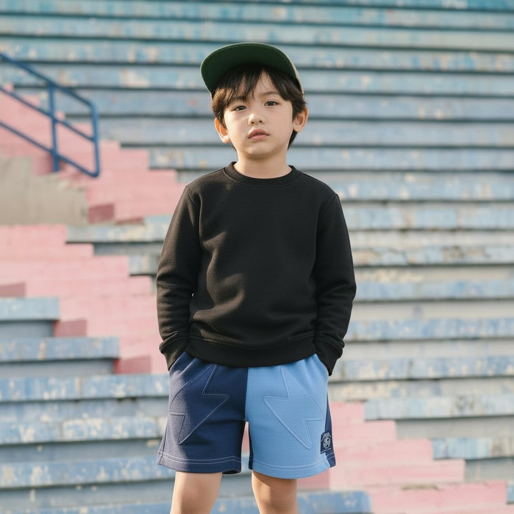 Child wearing a black sweatshirt and Blue Jogiel Lightning Shorts standing on bleachers.