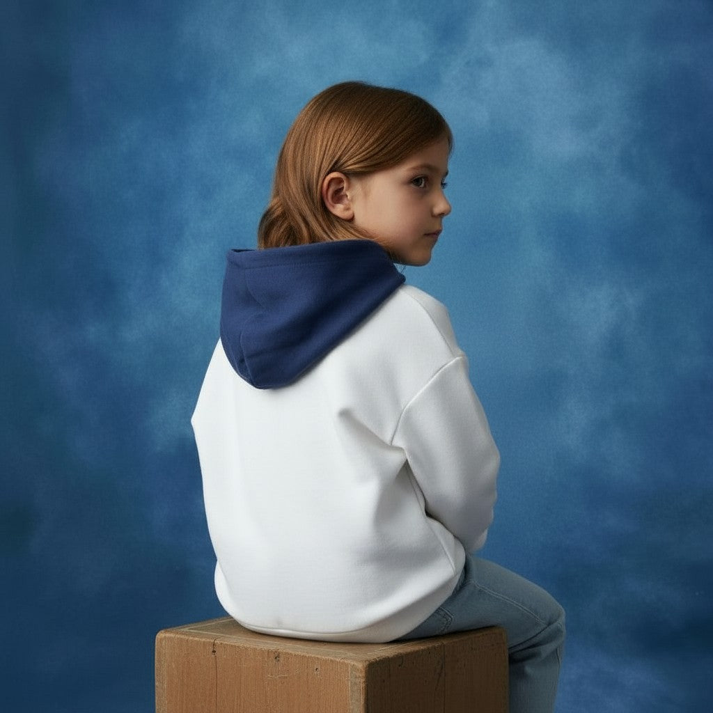 Child wearing a Blue Jogiel Reversible Varsity Hoodie on side B, a white hoodie with a blue hood sitting on a box against a blue background