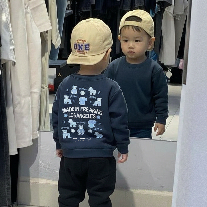 Toddler wearing a navy sweatshirt with embroidered text 'Made in Freaking Los Angeles' and animal graphics, standing in front of a mirror